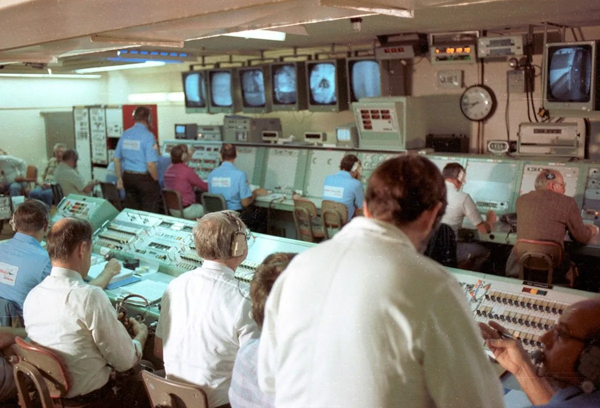 Operators at consoles and rows of television monitors in a launch control room.