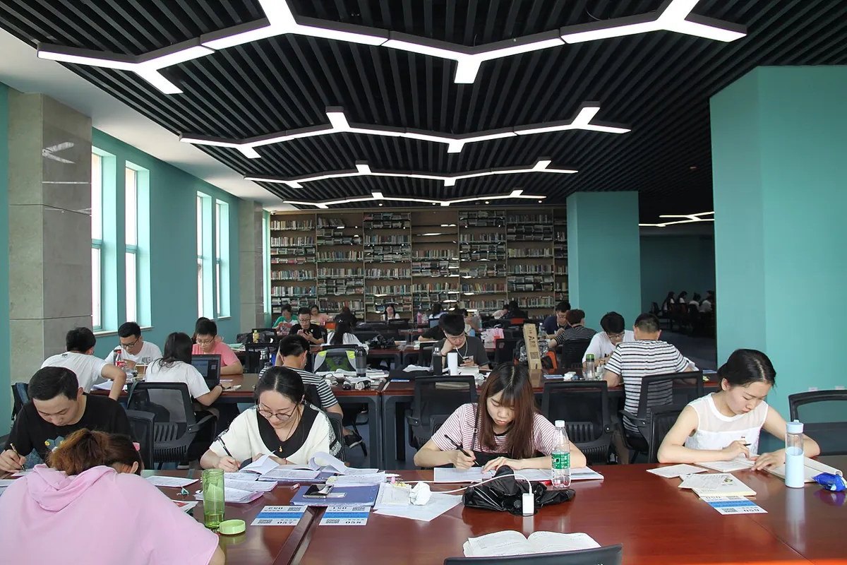 Students writing and reading at long tables in a university library.